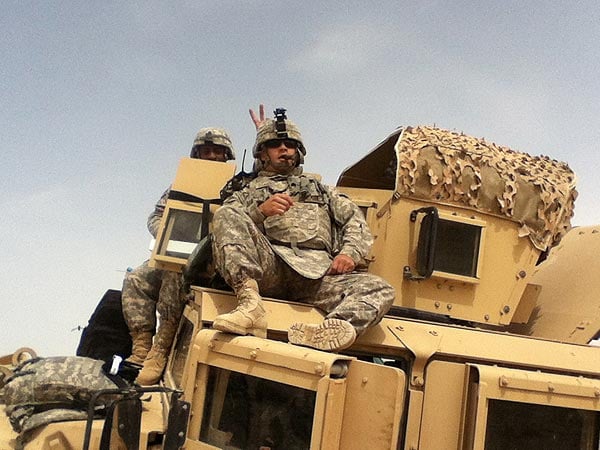 Spc. Carattini, M. relaxing on top of Humvee, while Staff Sargent Ried gives him bunny ears.