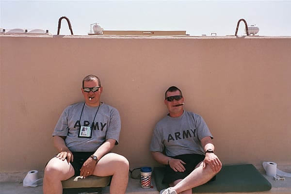 Two soldiers relax with a cigar while stationed in Iraq.